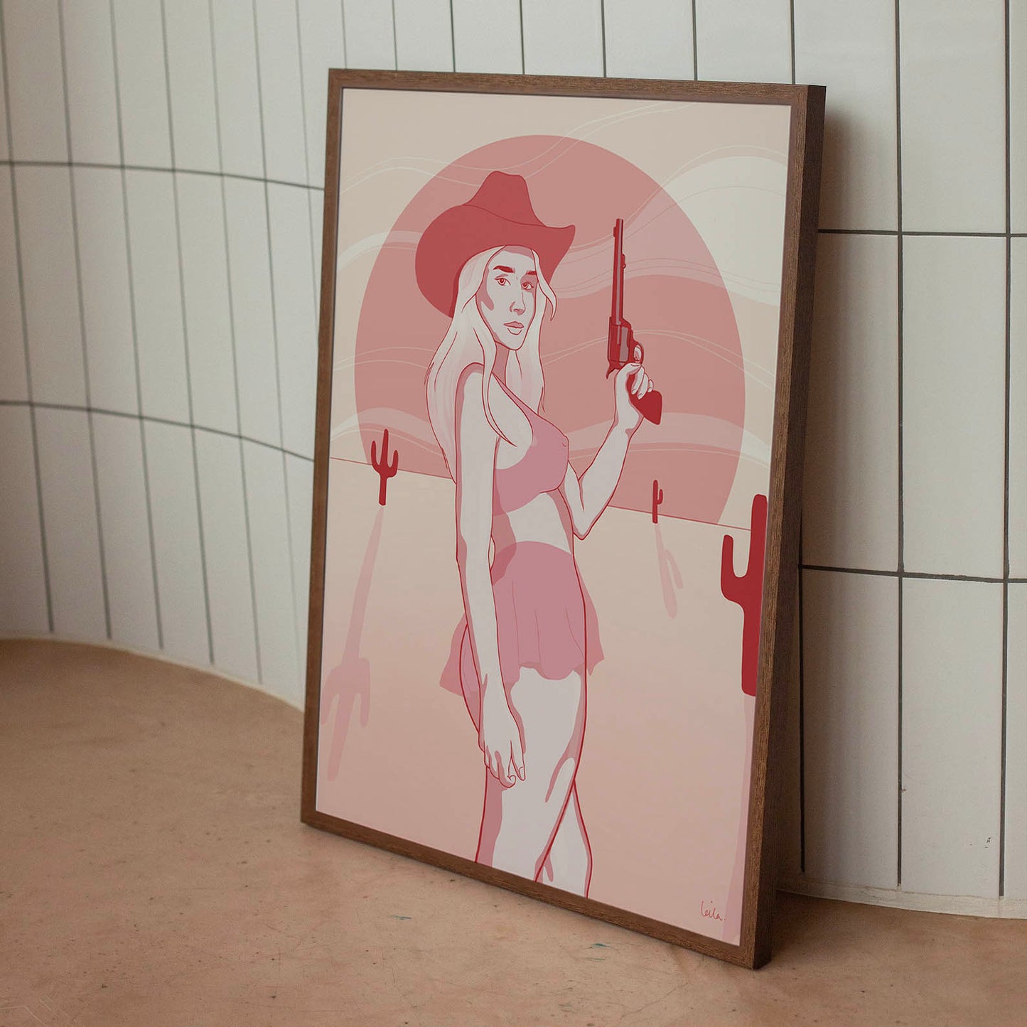 A framed poster depicting a digital drawing of a pink cowgirl in the desert, placed against a tiled wall.