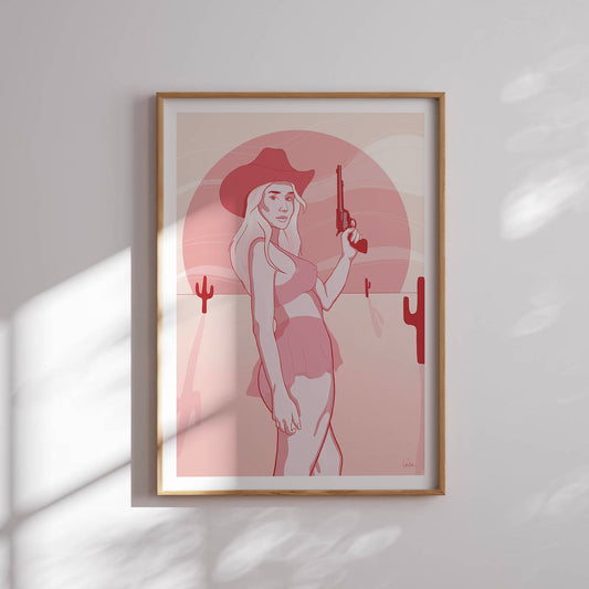 A framed poster depicting a digital drawing of a pink cowgirl in the desert, placed against a white wall.
