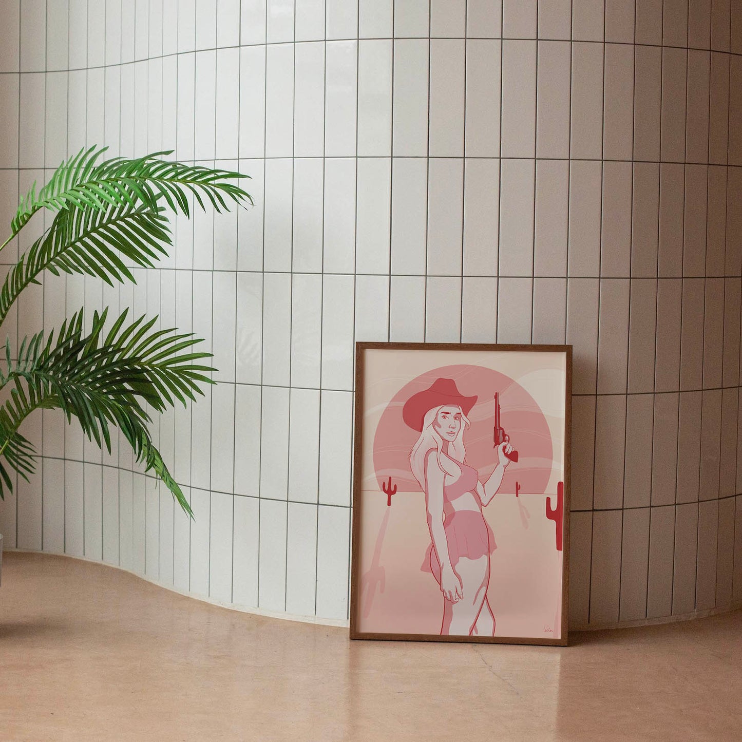 A framed poster depicting a digital drawing of a pink cowgirl in the desert, placed against a tiled wall.